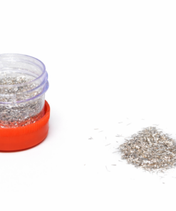 Clear plastic jar with a red base and a purple lid, filled with silver glitter, with a pile of loose glitter on the white surface beside it.