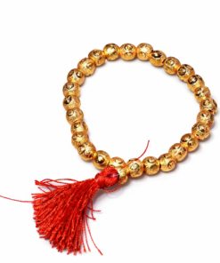Gold beaded bracelet with a red tassel hanging from it on a white background