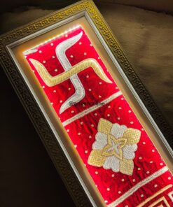 Framed red embroidered panel with gold and white snake-like curves and a white-gold floral motif, ornate gold frame visible on dark background.