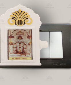 Small framed image of a Hindu deity mounted on a wall switch panel, with a white decorative frame and gold top ornament.