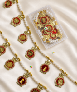Gold and red religious pendants with white bead strands scattered on satin fabric, next to a clear container of more pieces