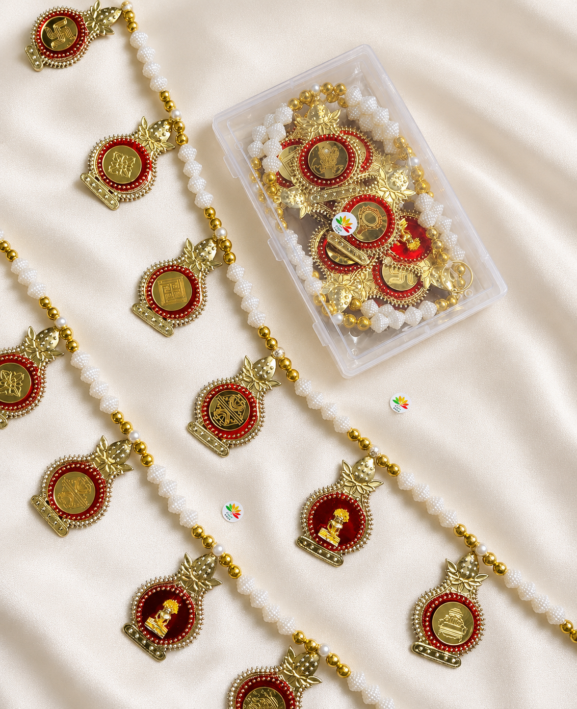 Gold and red religious pendants with white bead strands scattered on satin fabric, next to a clear container of more pieces