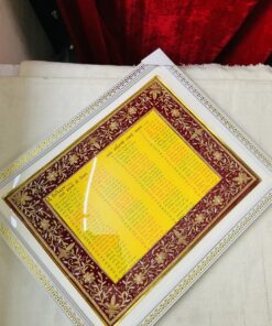 Ornate gold-and-red framed artwork with yellow text, displayed on light fabric beneath a red velvet backdrop.
