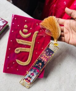 Pink velvet ceremonial card with gold embroidery and a golden tassel, held by a hand.