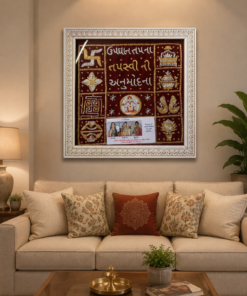 Framed maroon textile art with gold symbols and Gujarati script hanging above a beige sofa.
