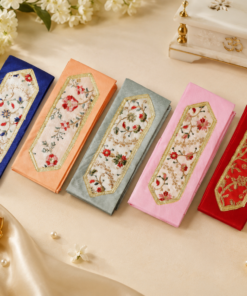 Colorful embroidered fabric pouches laid in a row on a beige surface, each with gold-bordered floral patches (blue, peach, gray, pink, red) for decorative use.