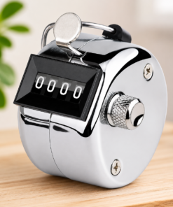 Silver handheld tally counter with four-digit display showing 0000 on a wooden surface.