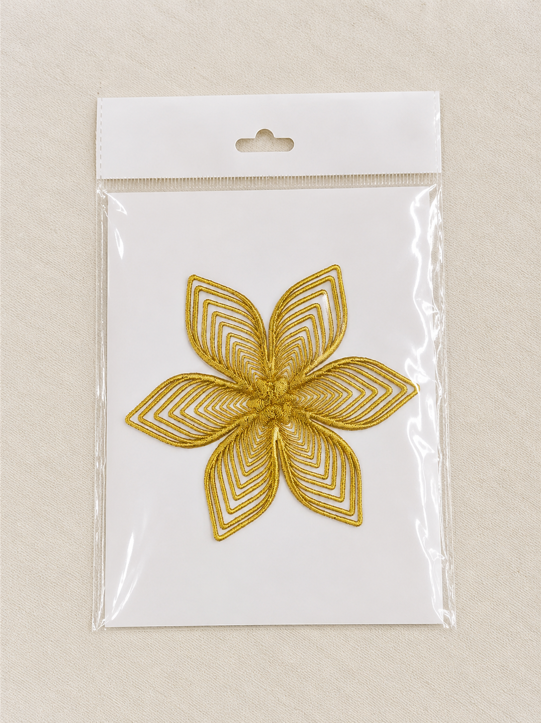 Gold embroidered five-petal flower patch in clear plastic packaging on a white backing.