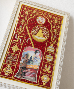 Framed decorative red velvet textile with gold embroidery and floral motifs, displayed in an ornate white frame.