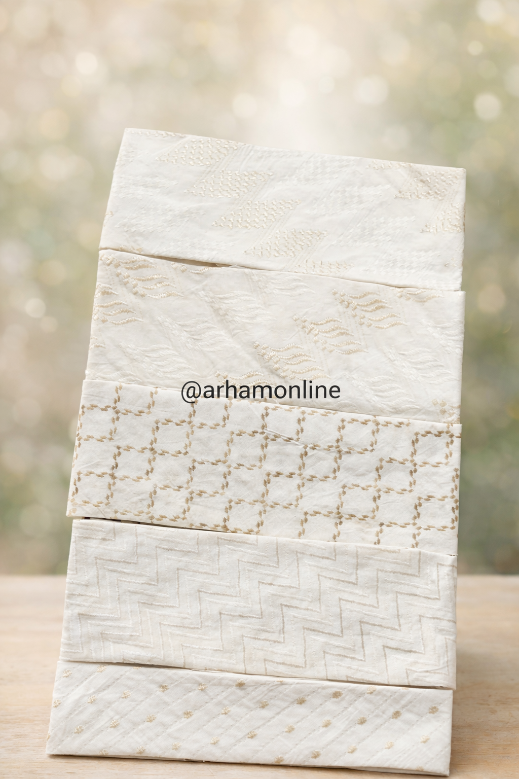Stack of cream fabric swatches with subtle embroidered patterns arranged in a tower on a wooden surface