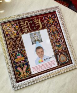 Ornate decorative frame surrounding a photo of a man with Gujarati text beneath it and colorful embroidery panels on the sides.