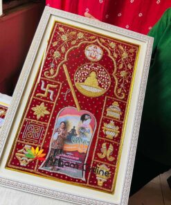Framed red embroidered textile art with gold motifs and a central arched photo panel, decorative temple-themed design.