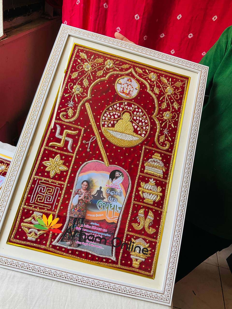 Framed red embroidered textile art with gold motifs and a central arched photo panel, decorative temple-themed design.