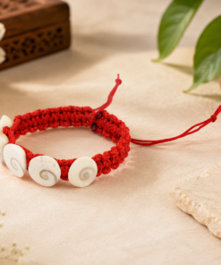 Red knotted bracelet with white spiral-shell beads on a beige surface.