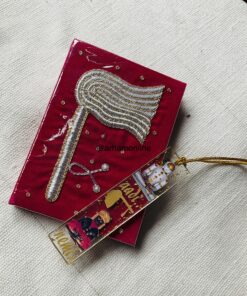 Red velvet card featuring a braided silver feather brooch with gold edging, set on light fabric background.