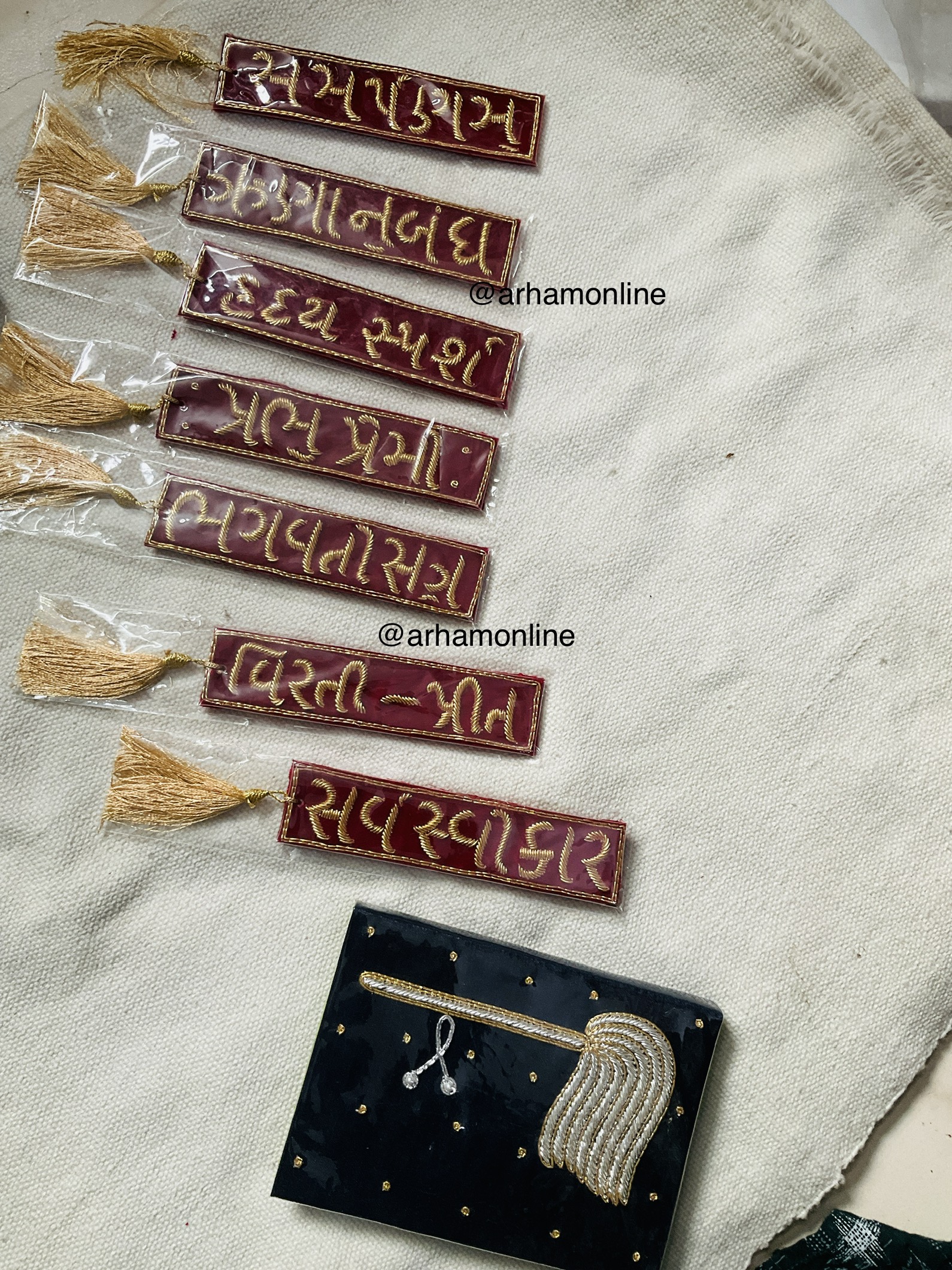 book mark Row of maroon fabric tags with gold embroidery and gold tassels on a light woven cloth.