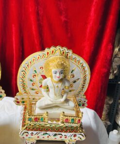 Ornate white statue of a seated meditating figure with gold adornments on a decorated pedestal, red velvet backdrop.