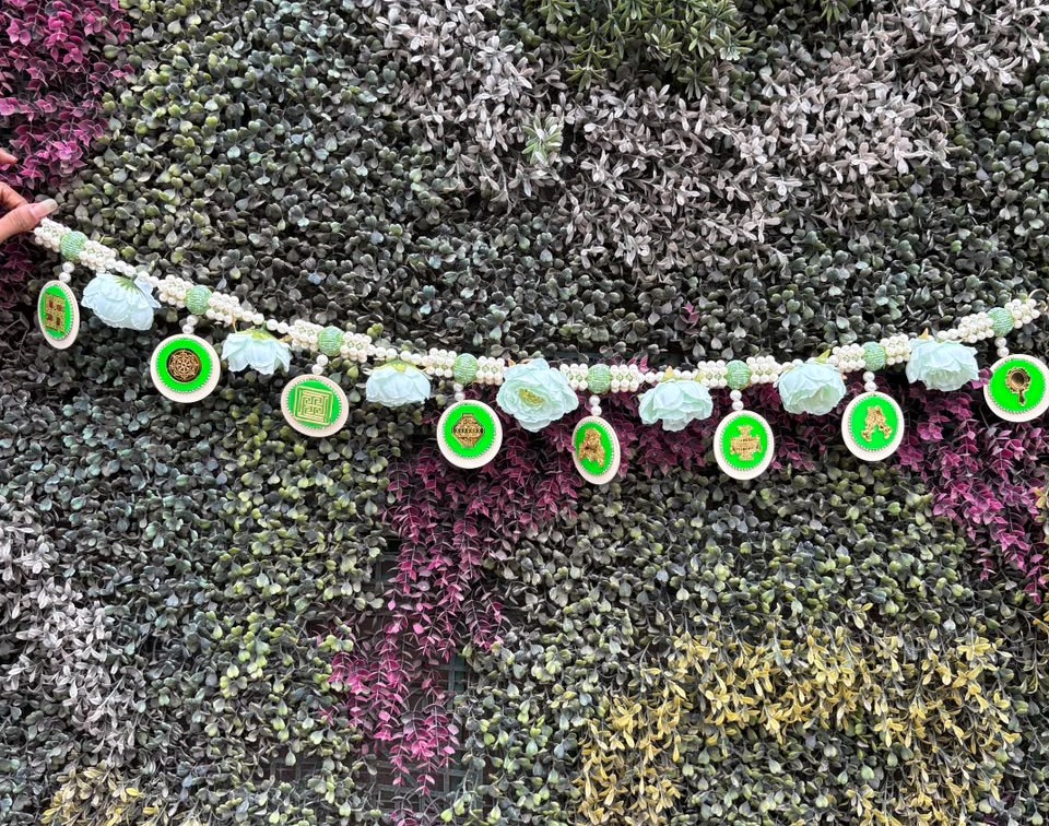 Toran green 1 Decorative bead garland with round green-medallion charms draped across a colorful succulent wall.