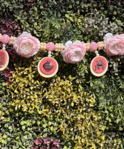 Decorative garland with large pink paper roses and pink beaded ornaments against a lush green leafy backdrop.