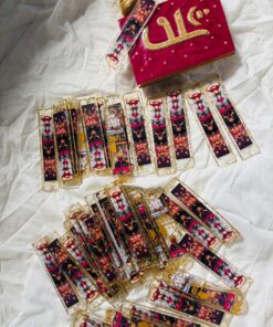 Row of gold-edged decorative bookmarks with colorful figures, spread on white fabric beside a red velvet box with gold embroidery.