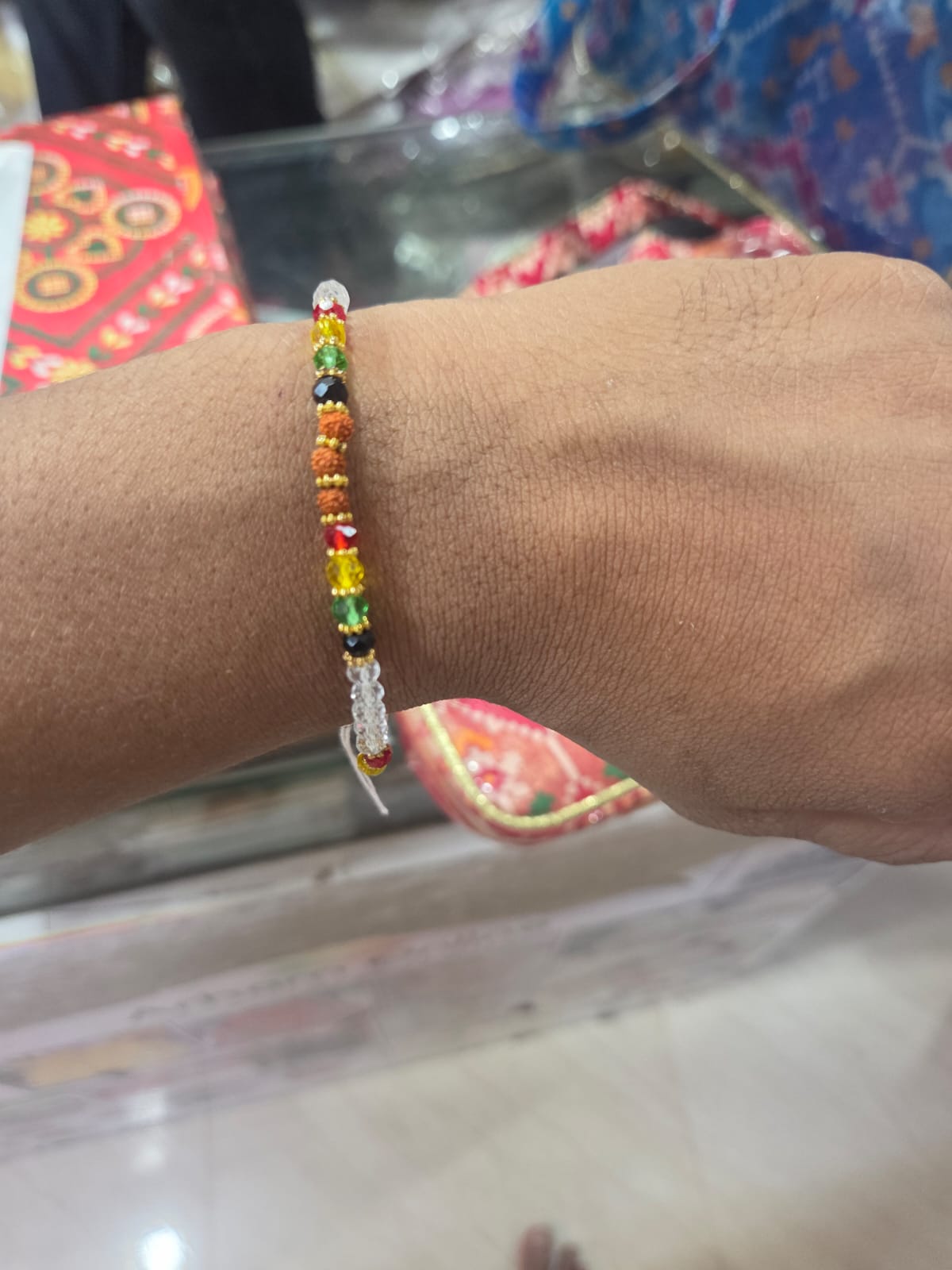 WhatsApp Image 2026-07-17 at 11.18.19 AM Beaded bracelet with multicolor stones (red, yellow, green, orange, black) worn on a brown wrist indoors.