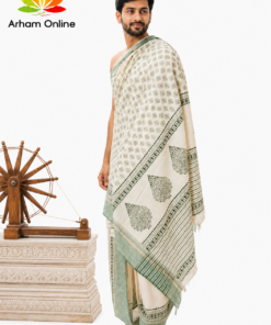 Man modeling a cream and mint saree with geometric patterns, standing barefoot beside a wooden spinning wheel; Arham Online logo in the top-left corner.